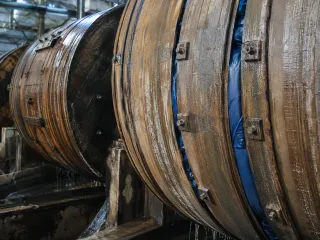 Dos bombos de madera en fila dentro de la planta de curtido, con las duelas mojadas y el agua escurriendo por debajo