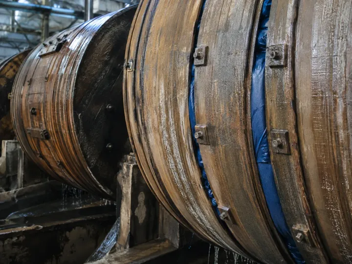 Dos bombos de madera en fila dentro de la planta de curtido, con las duelas mojadas y el agua escurriendo por debajo